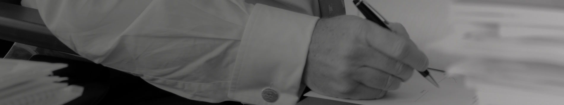 Black and white close-up of a hand in a formal shirt, signing a document.
