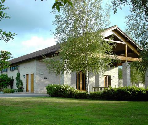 A large modern house made of stone, with a tiled ceiling, in a green garden.