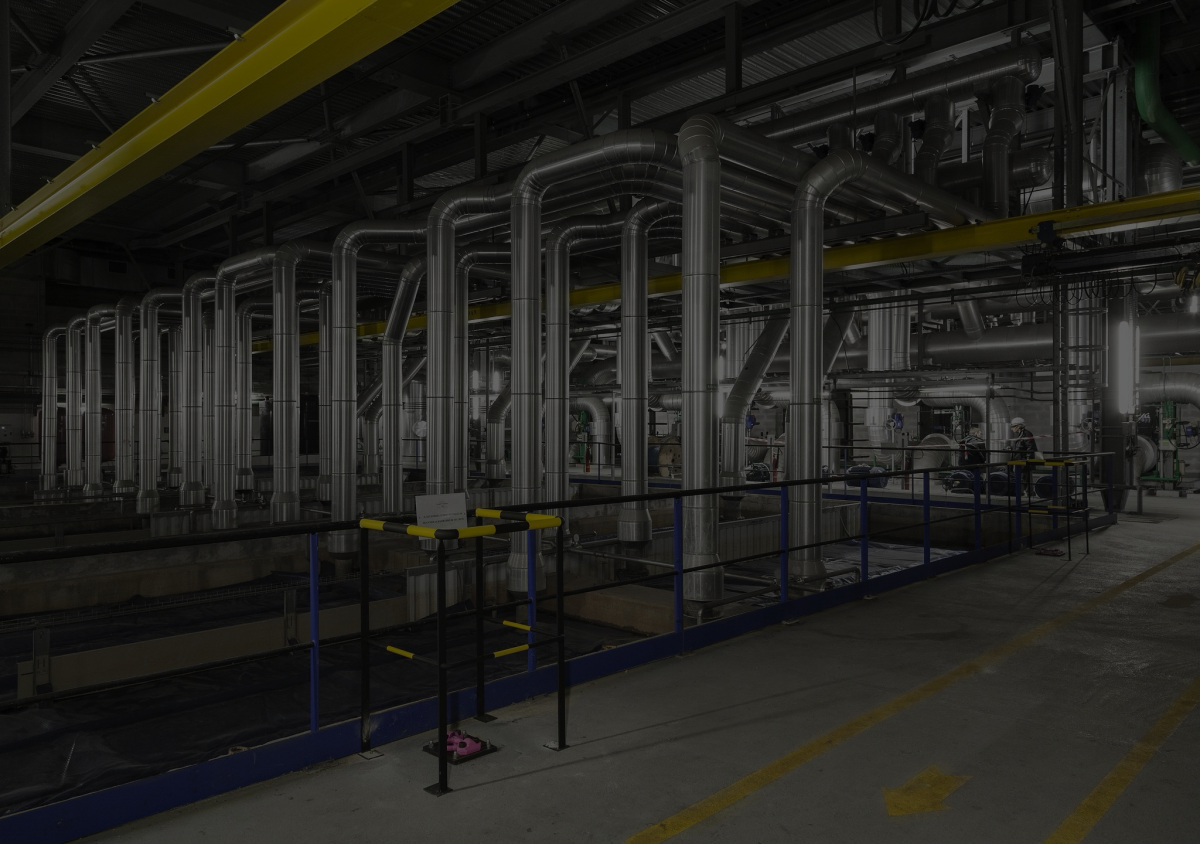 A large, dimly lit factory, featuring floor to ceiling metal pipes.
