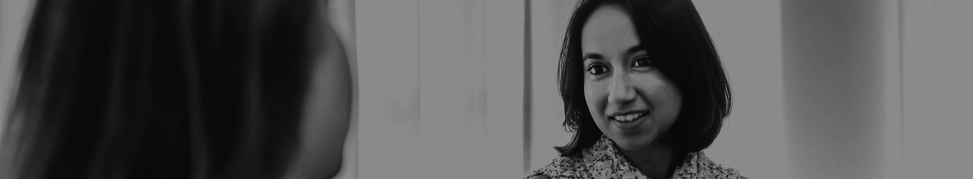 Black and white image of a young woman, looking intently at her interlocutor, whose back of the head is visible in the foreground.