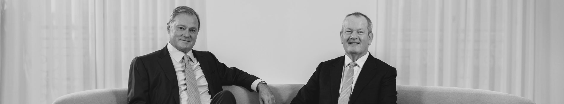 Black and white image of Antin Co-Founders Alain Rauscher and Mark Crosbie in suits on a sofa.